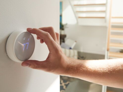 Hand adjusting a round, white smart thermostat on a white wall in a home.