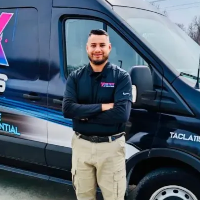 Man in black shirt and khaki pants stands in front of a company van with arms crossed.