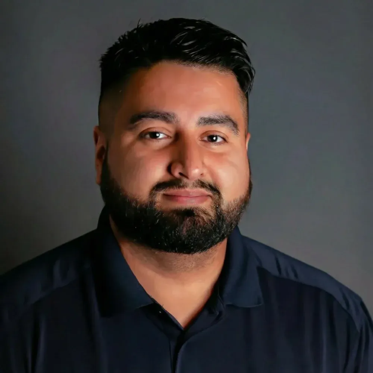 Man with dark hair and beard, wearing a navy polo shirt, smiles at the camera.