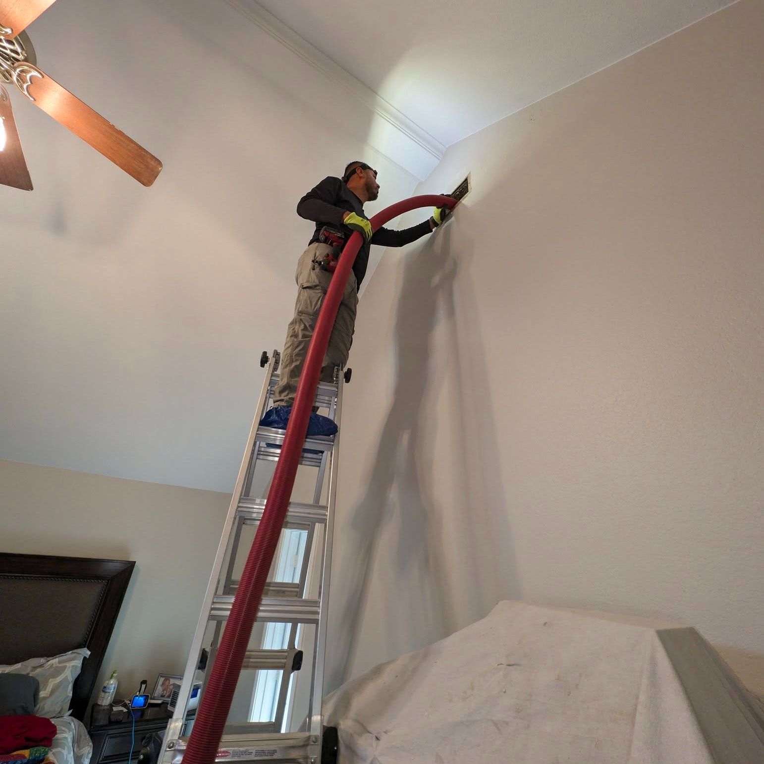Man on ladder spraying insulation on a high interior wall.