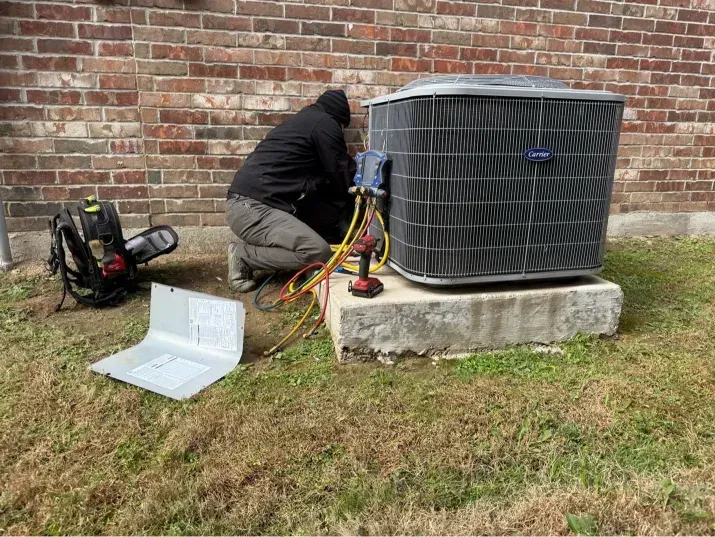 HVAC technician working on an AC unit outside a brick building.