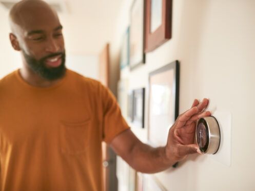 Man adjusting a smart thermostat on a wall in a home hallway.