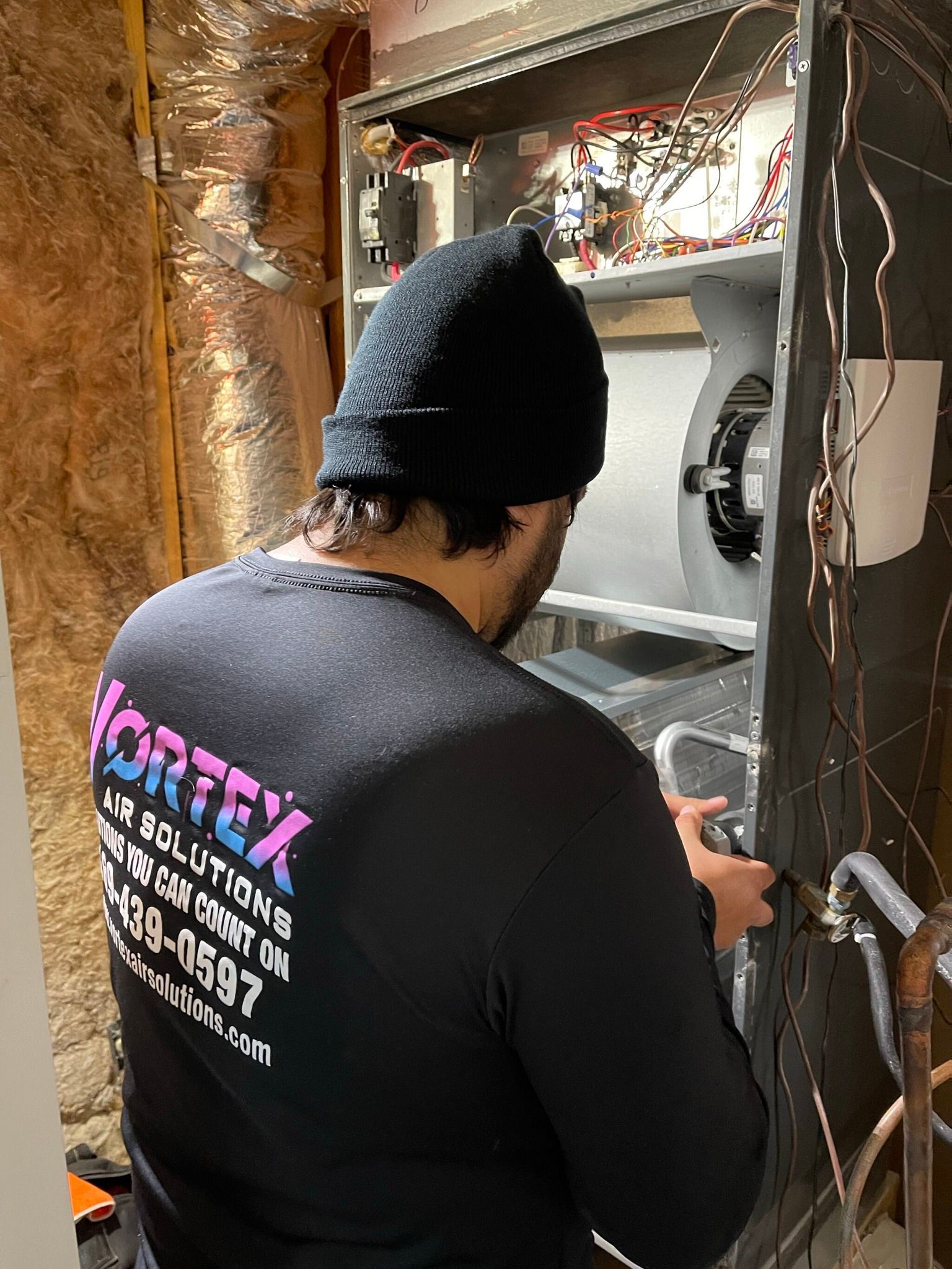 Person in black beanie and shirt working on HVAC system. The shirt has 