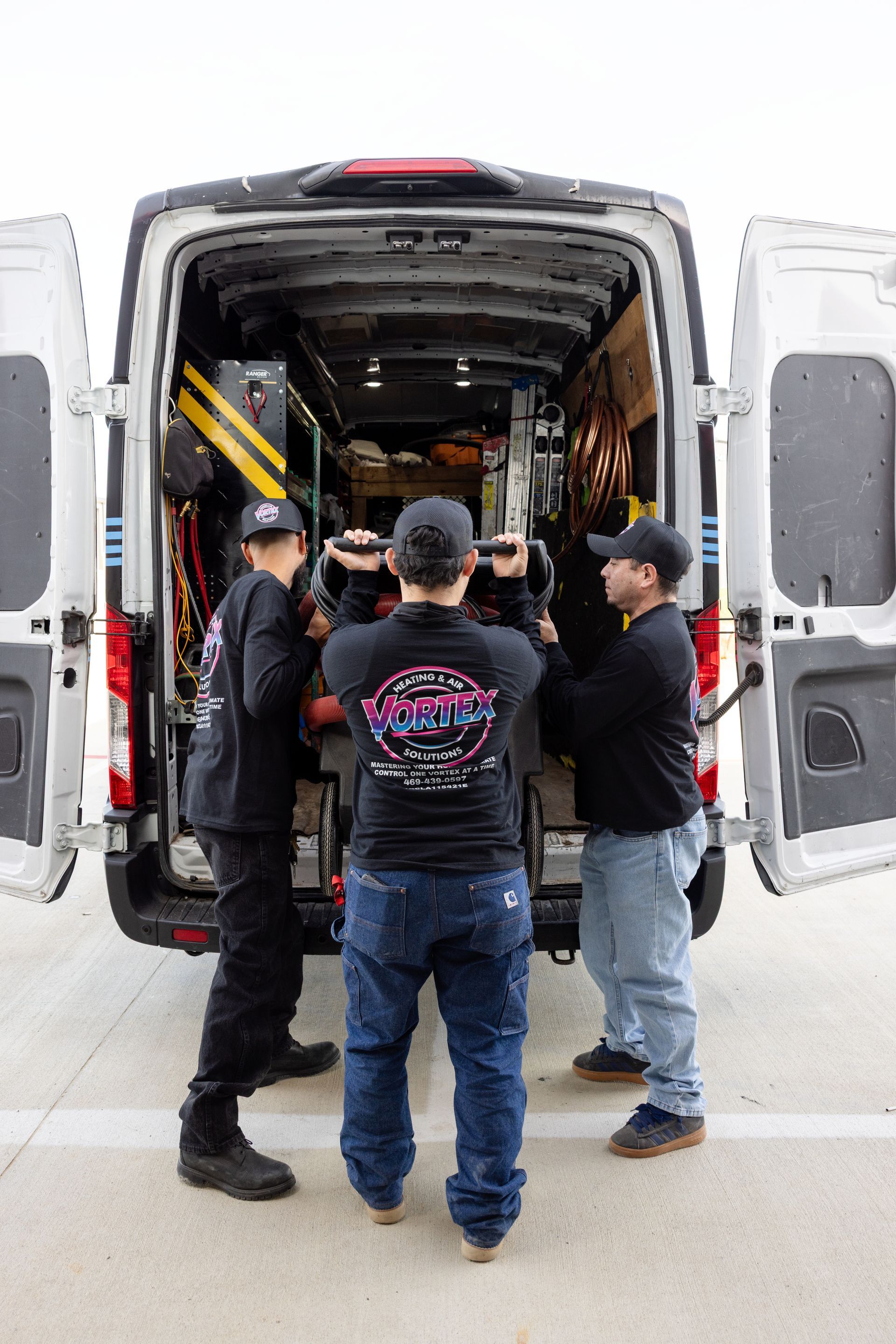 Woman adjusting a smart thermostat, using a smartphone. In a home interior, near a kitchen.