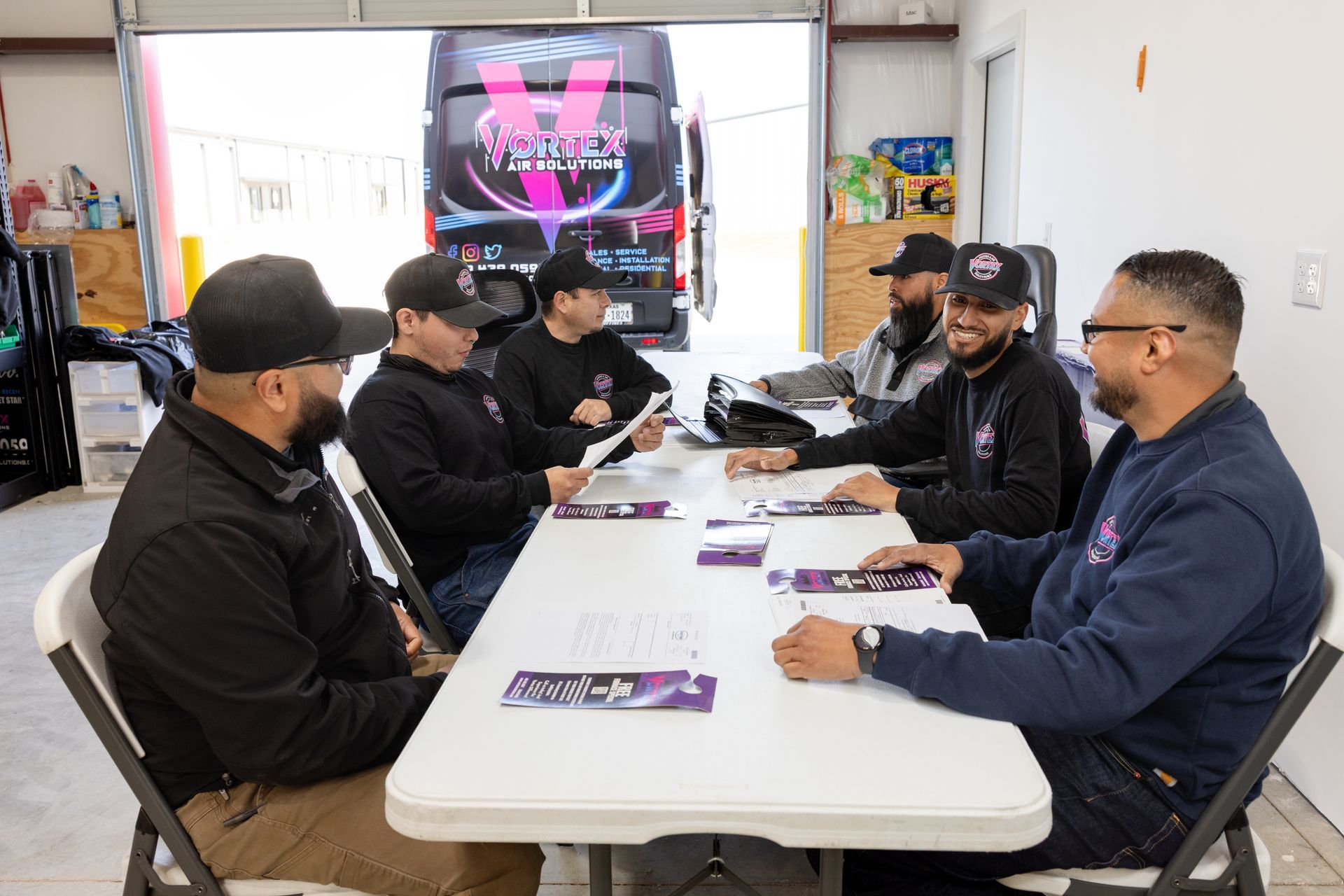 Family on a sofa with laptop, two children playing in kitchen. Smiling, light-filled room.