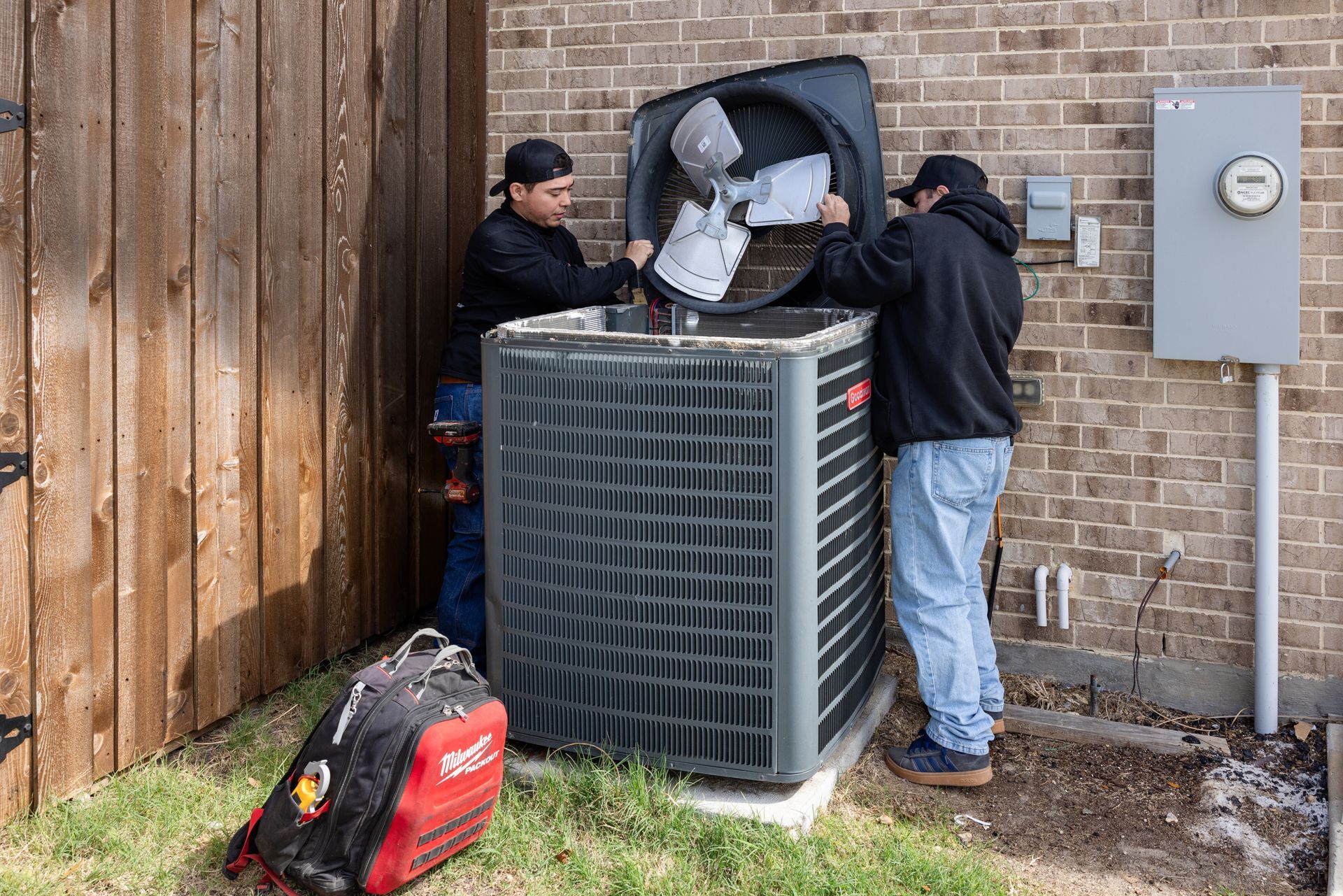 HVAC technician inspecting an air conditioning unit outside a brick building.