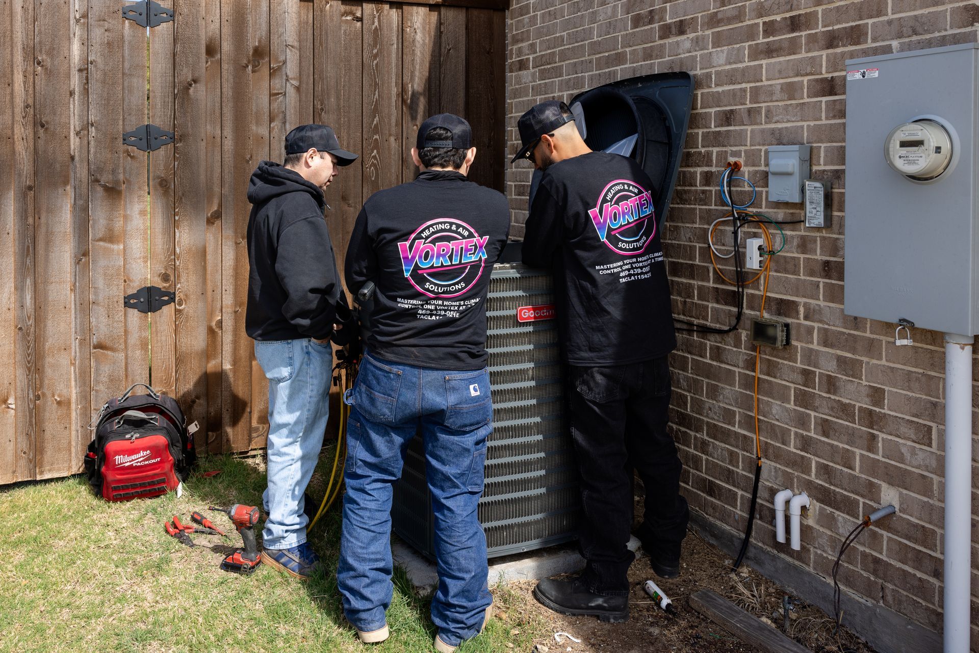 Person working on HVAC ductwork in an attic, wearing a hard hat, kneeling and using tools.