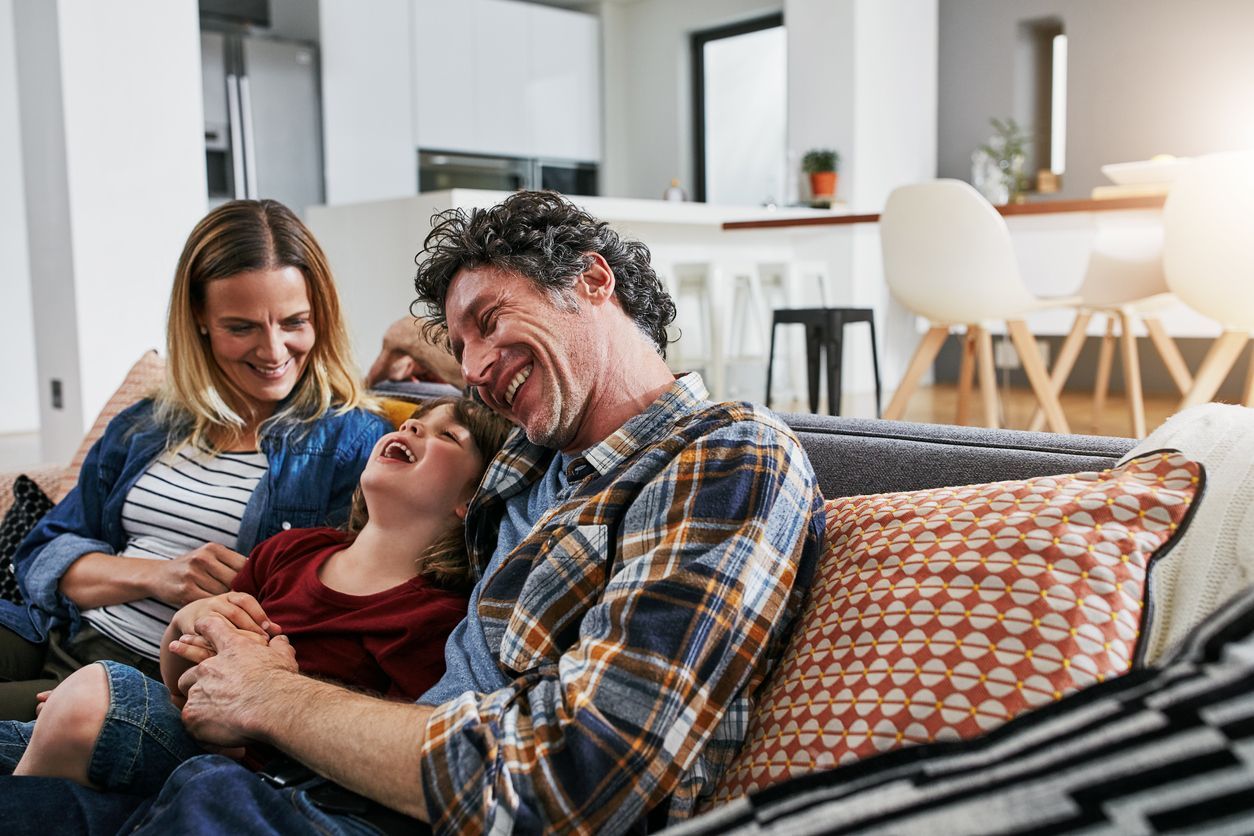 Family laughing together on a couch in a bright living room.