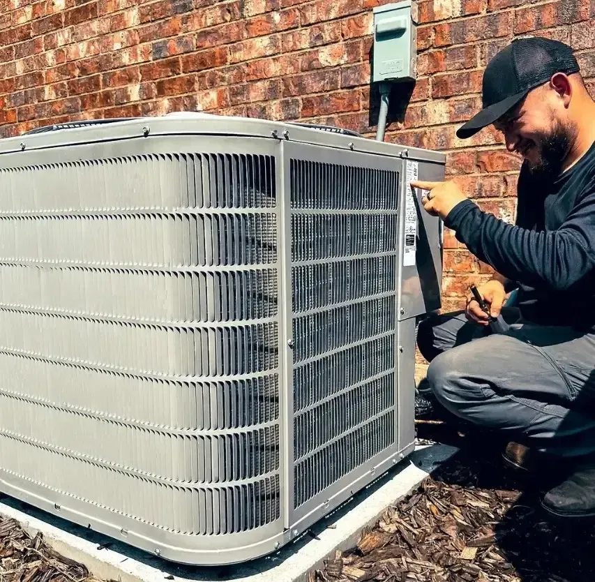 HVAC technician examining an air conditioning unit outside a brick building.