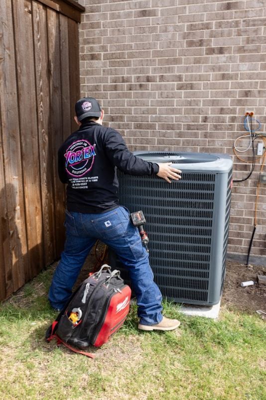 Three air conditioning units outside a building with electrical meters and bushes.
