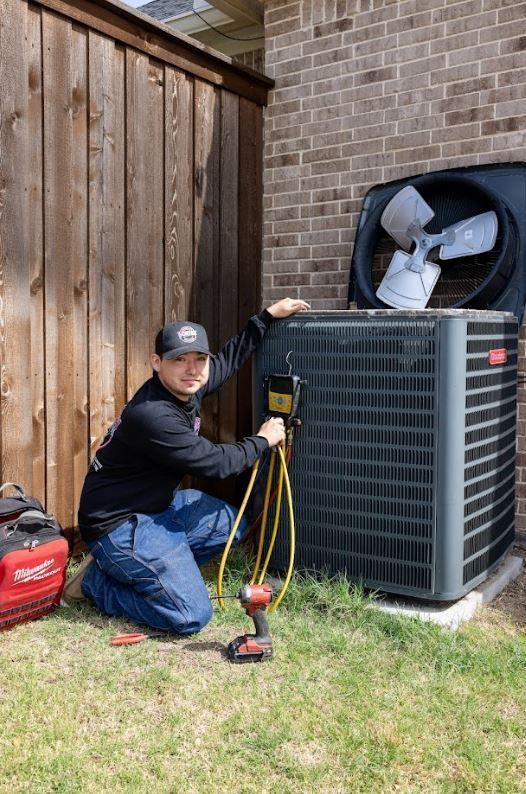 Two air conditioning units on gravel next to a wooden fence.