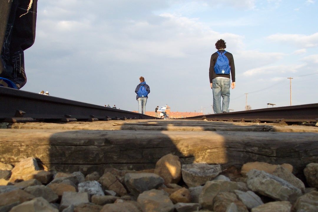 A man with a blue backpack is walking on the train tracks to Auschwitz