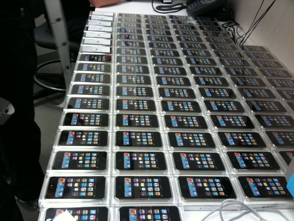 Dozens of identical smartphones laid out in neat rows on a table in an indoor setting.