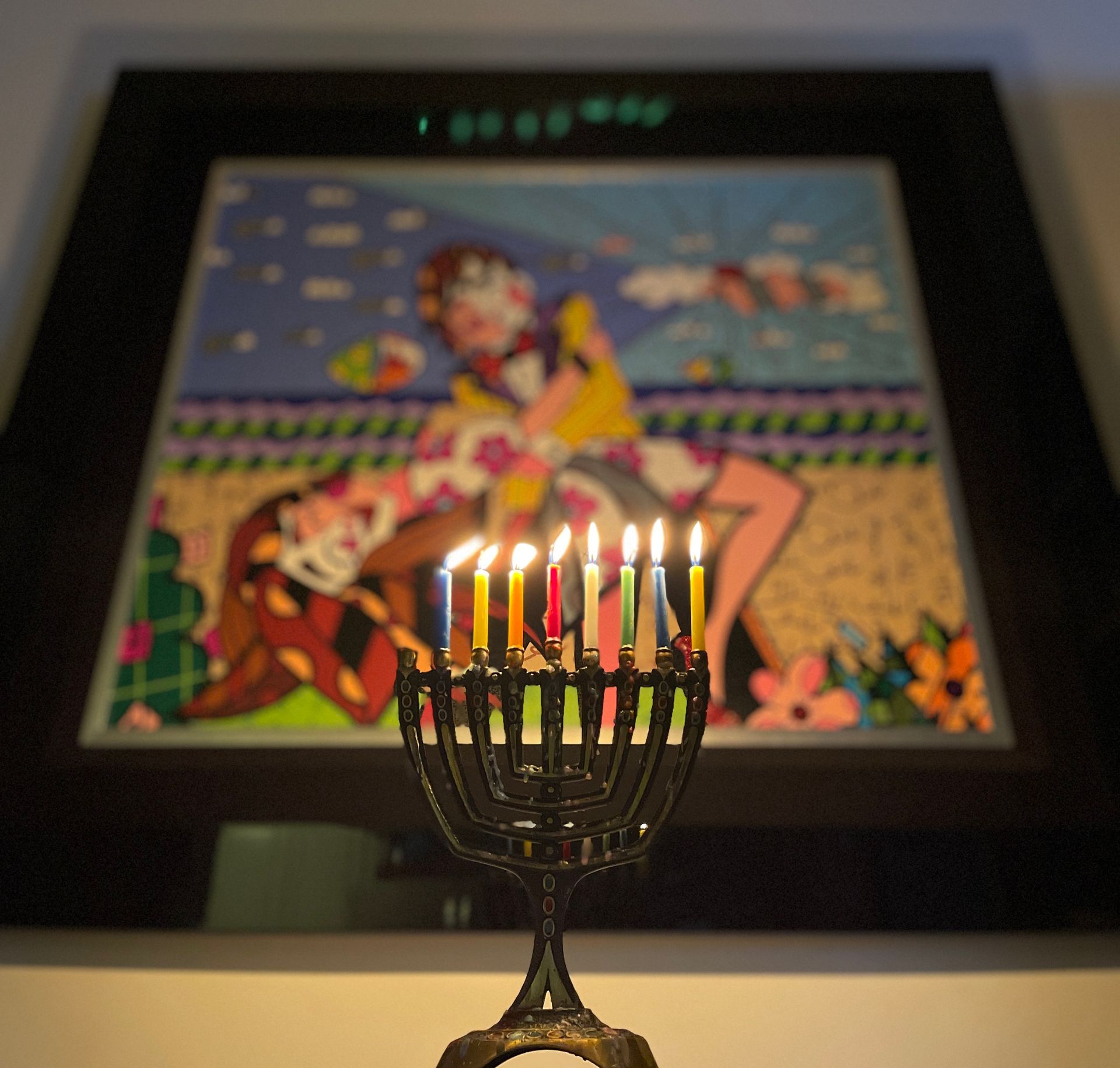 A menorah with lit candles in front of a painting.