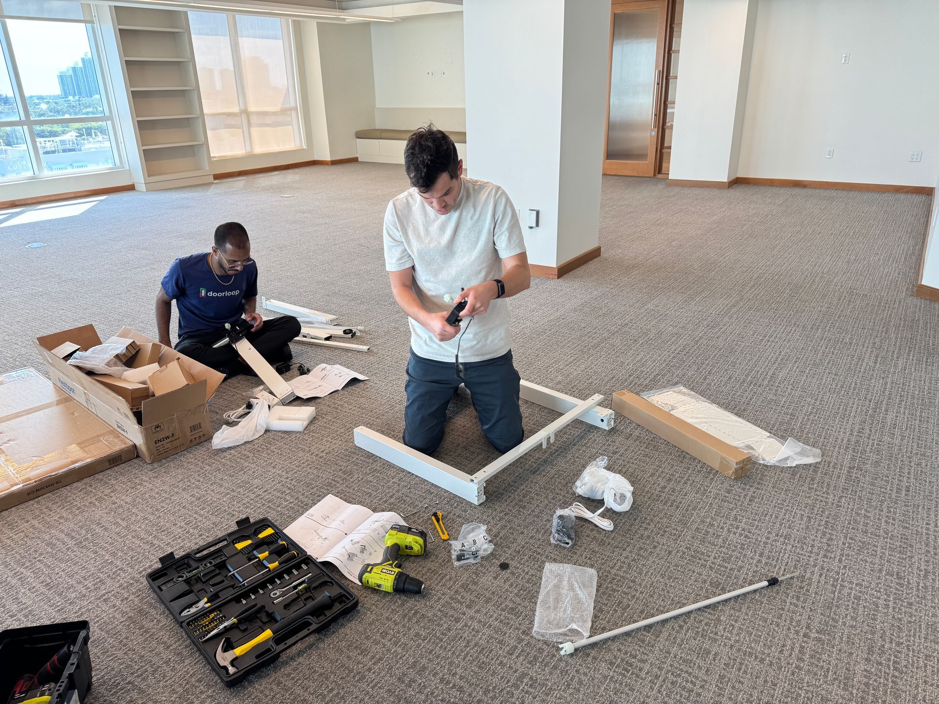 Two men are kneeling on the floor working on a table.