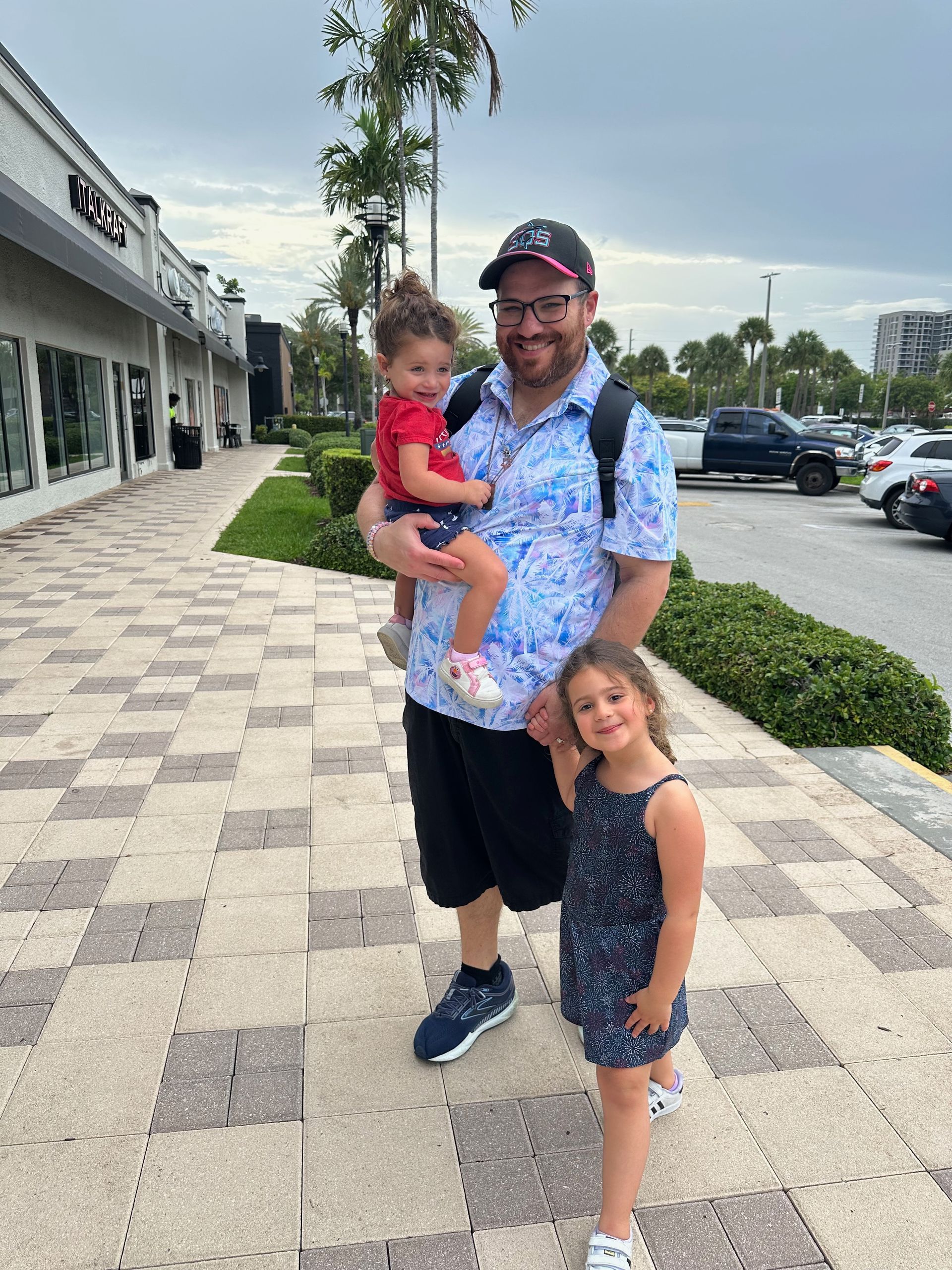 A man is holding a baby and two little girls on a sidewalk.