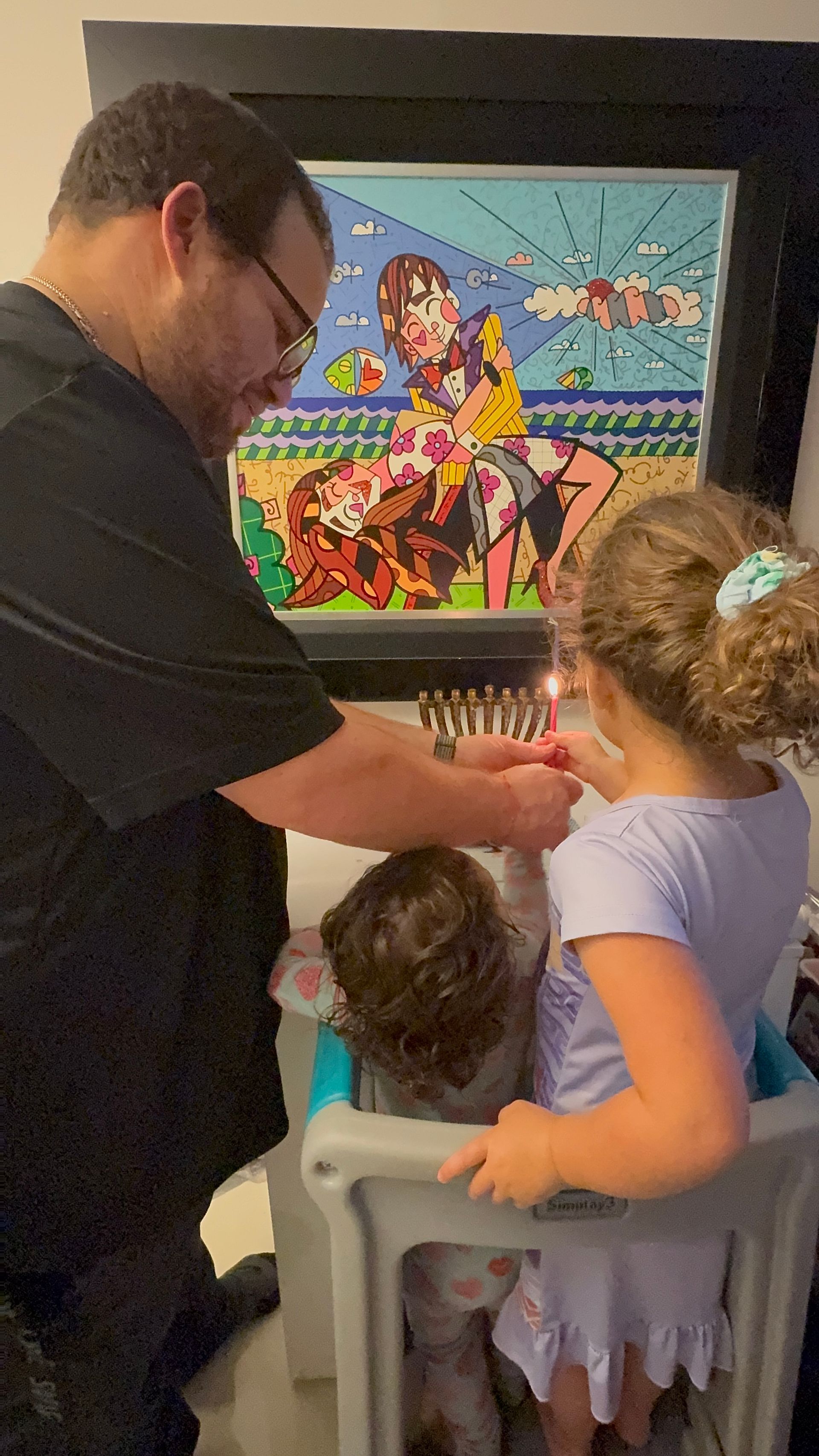 A man is lighting a candle for a little girl in a high chair.