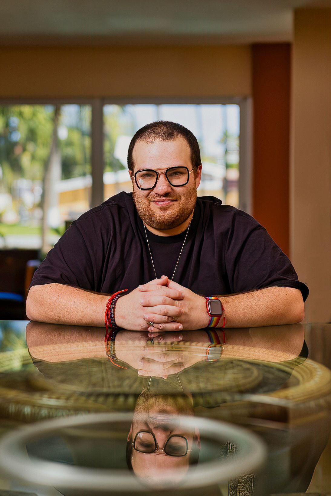 A man with glasses is sitting at a table with his hands folded.