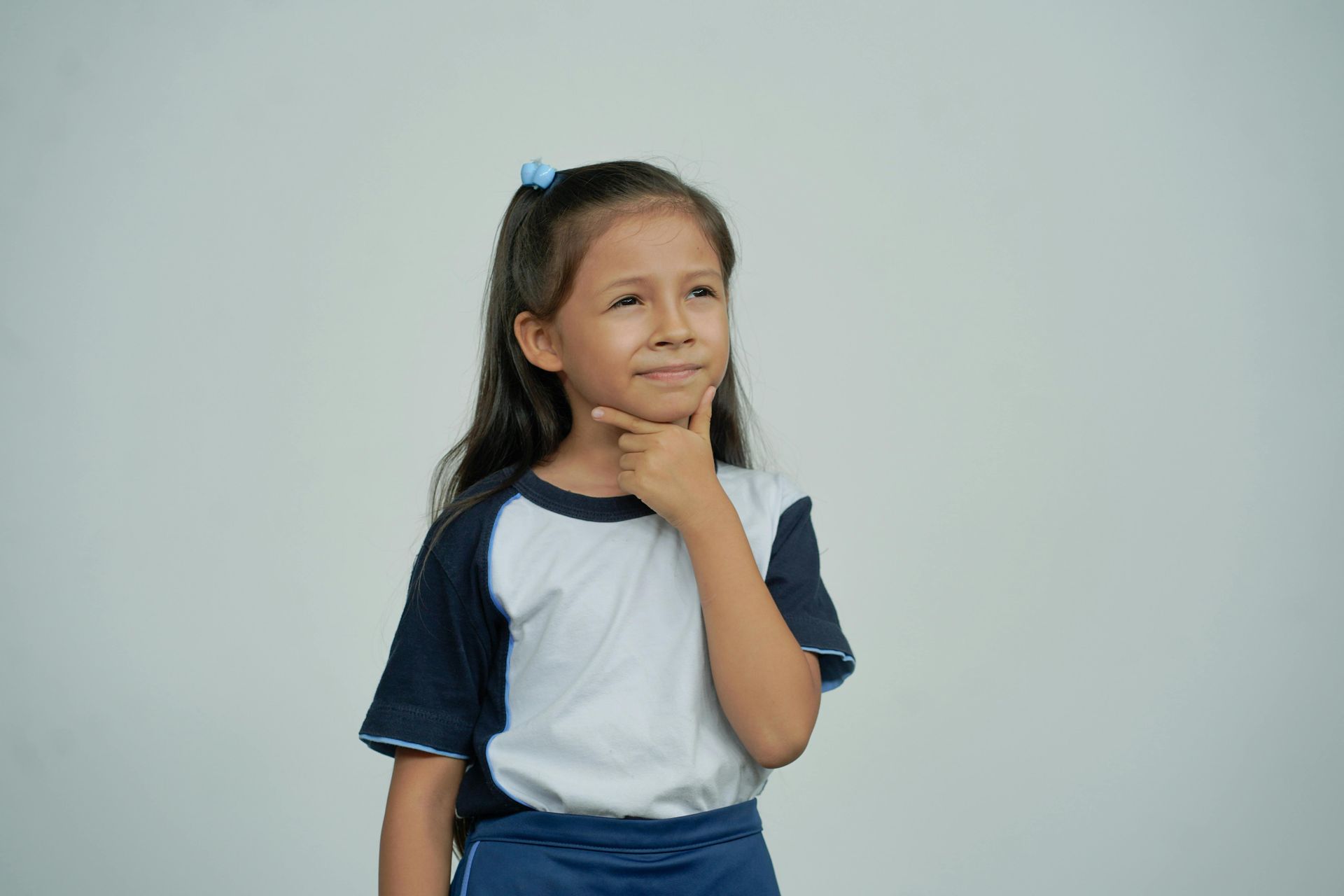 A little girl is thinking with her hand on her chin.