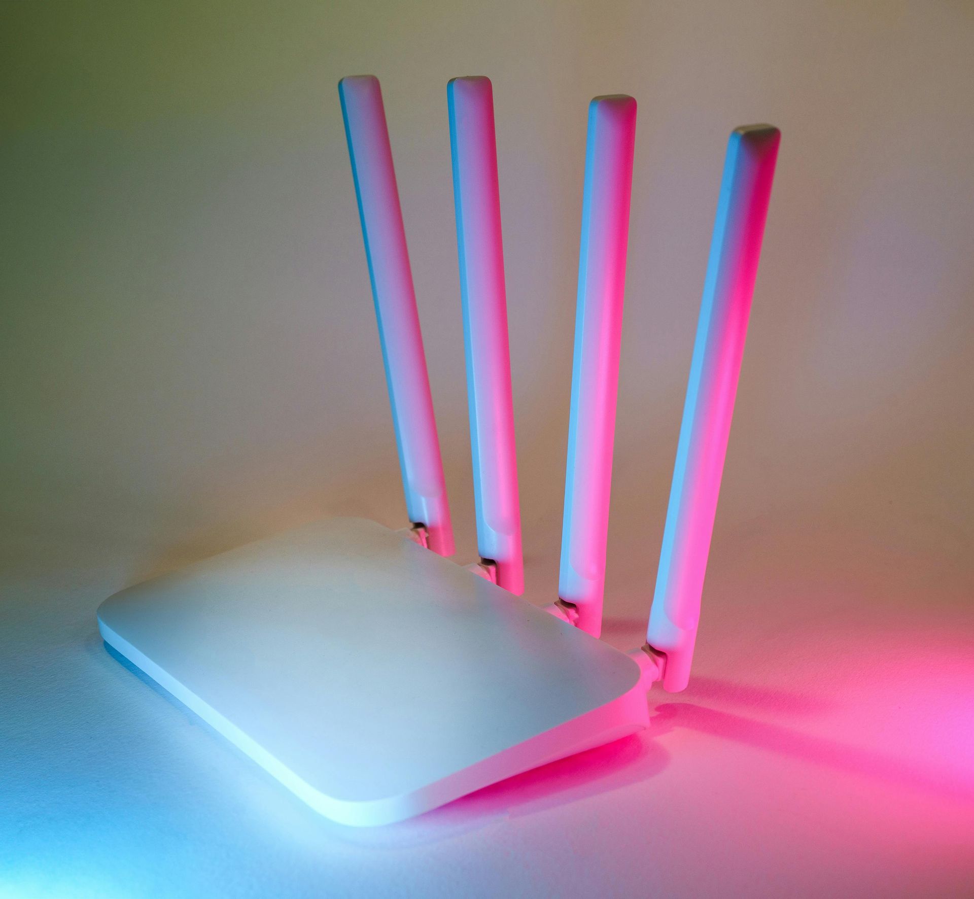 A white router with pink and blue antennas is sitting on a table.