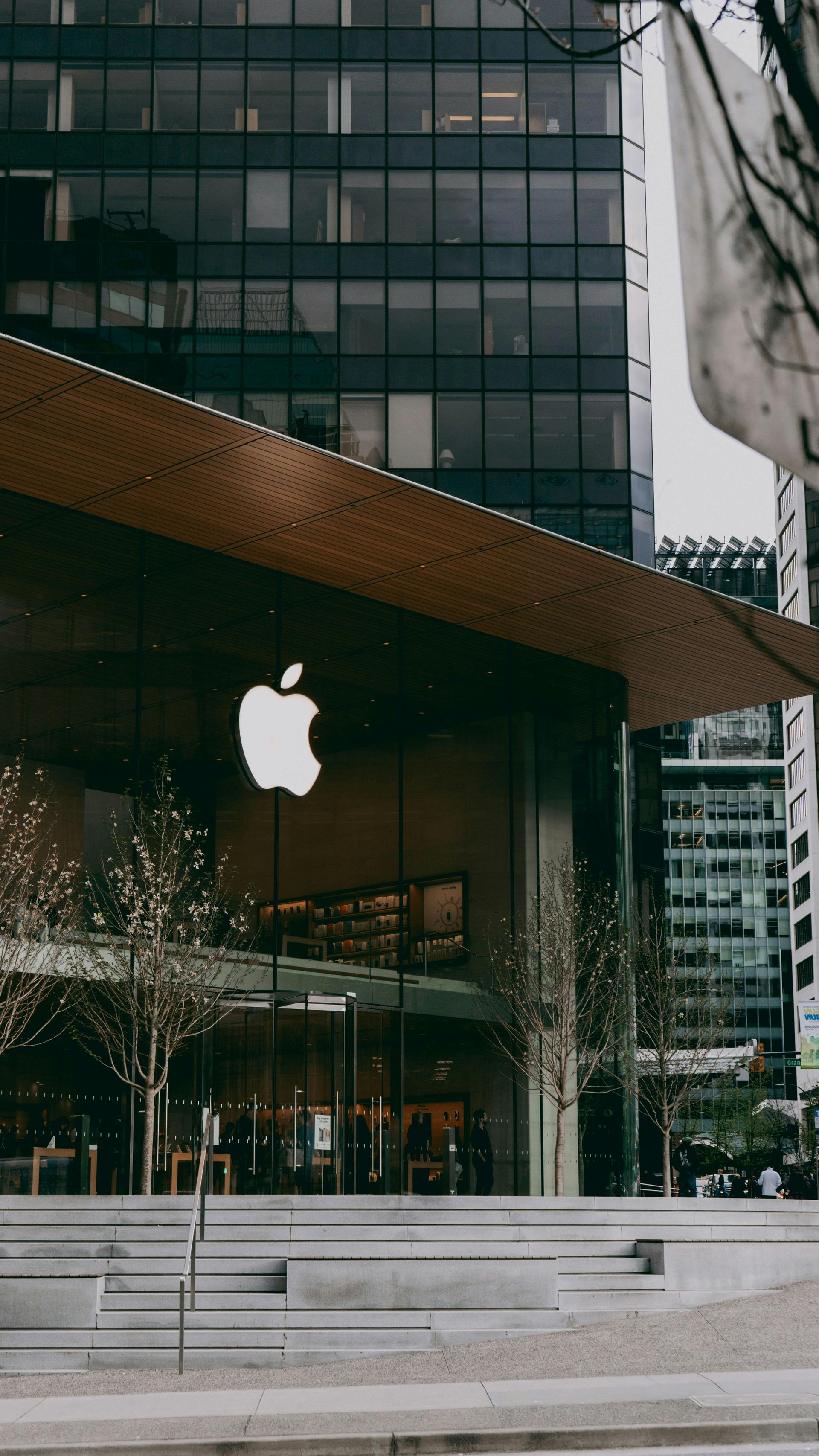 The exterior of an Apple Store featuring a large, glowing white apple logo set against a building with a tiered staircase.