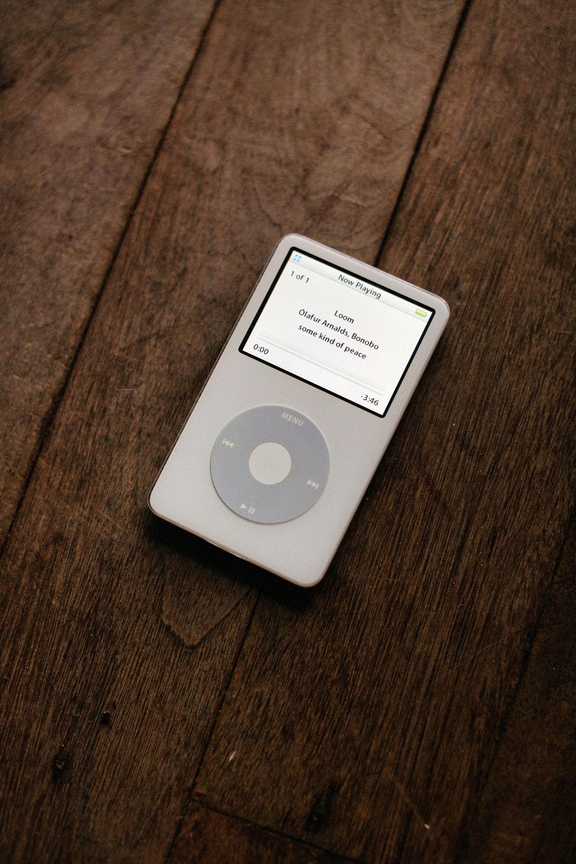 A white iPod classic sitting on a dark wooden plank floor.