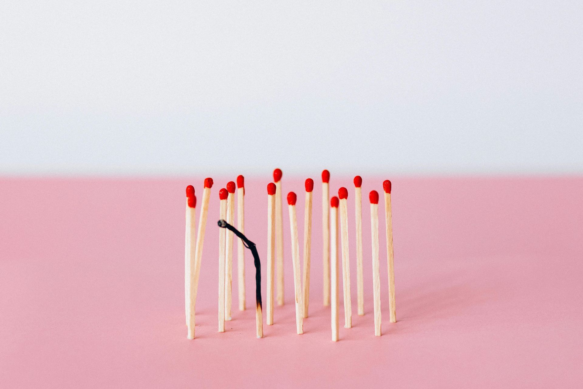 A bunch of matches are lined up in a row on a pink surface with one burnt-out.