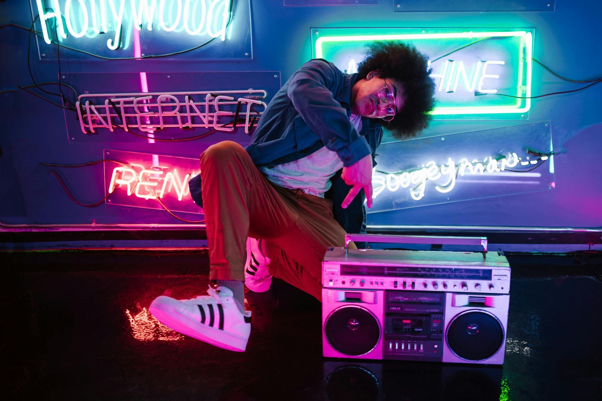 A man is dancing in front of a neon sign while holding a boombox.