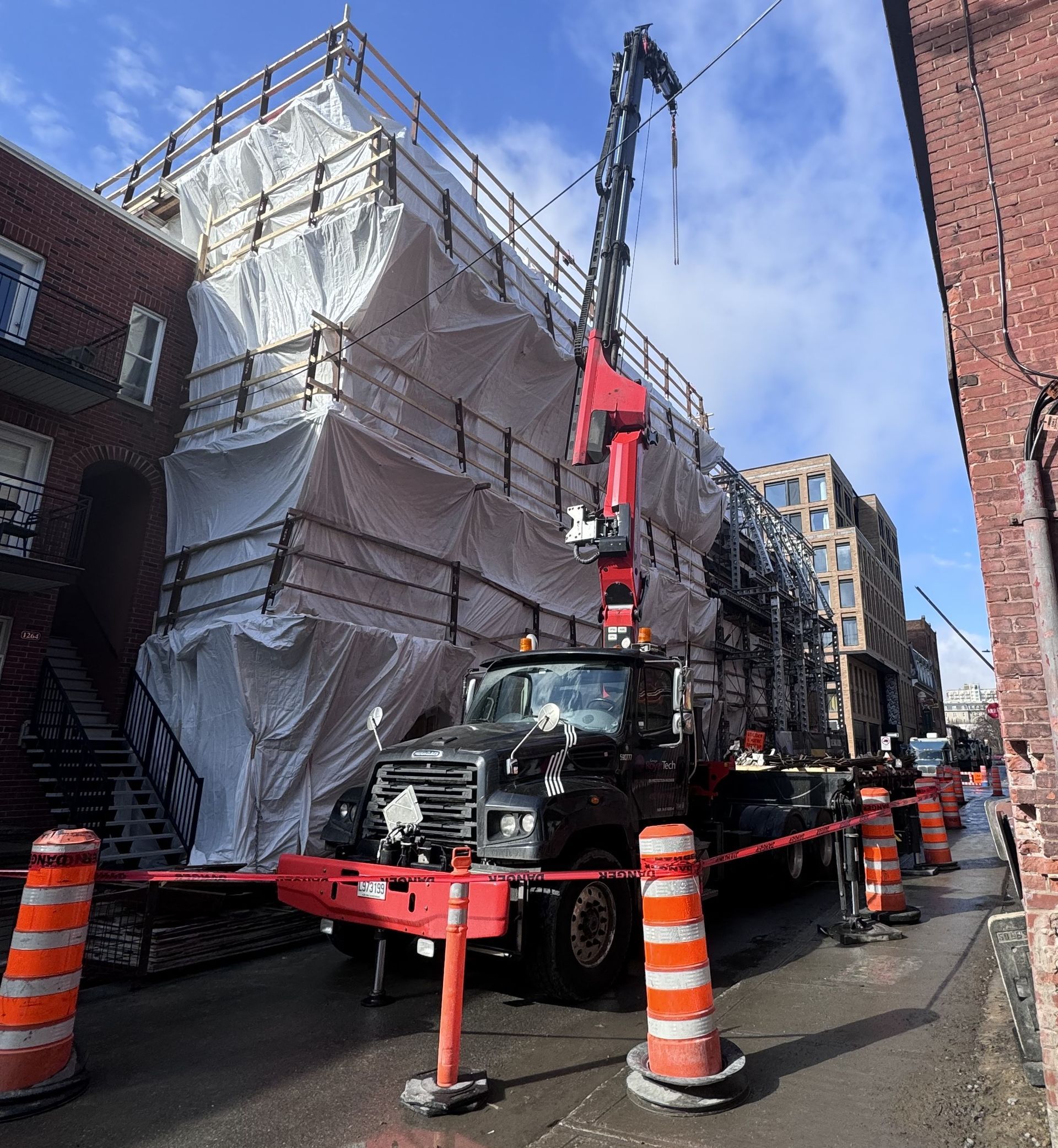 A truck with a crane attached to it is parked in front of a building covered in tarps.