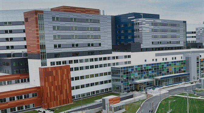 An aerial view of a large hospital building with a soccer field in front of it.