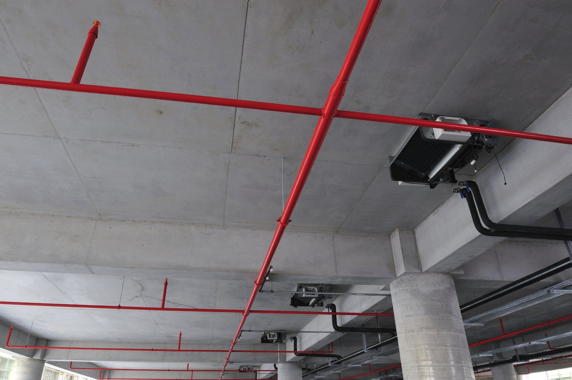 Des tuyaux rouges sillonnent un plafond en béton. Des conduits et des câbles noirs sont également visibles.