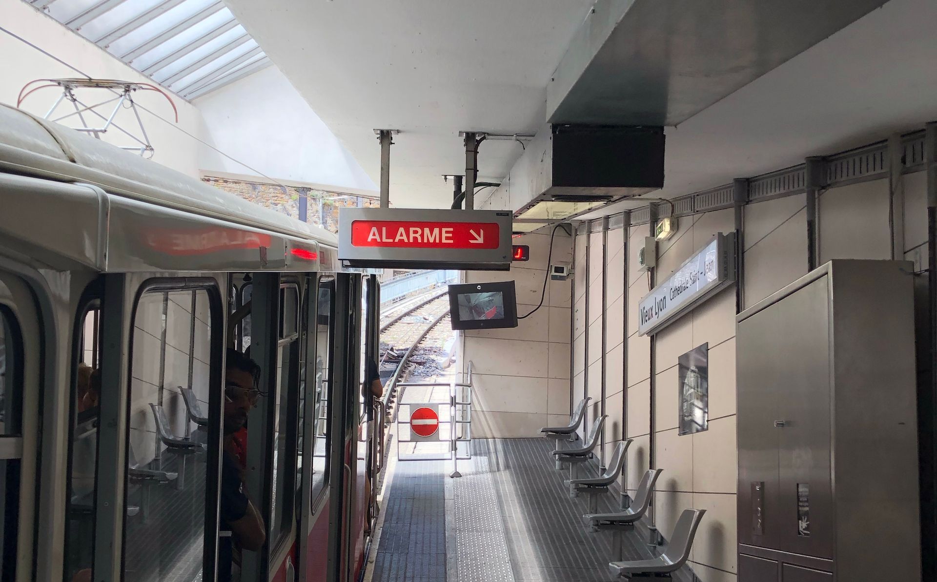 Un funiculaire sur le quai d'une gare, avec un panneau d'affichage numérique rouge au-dessus indiquant le mot « ALARME ».