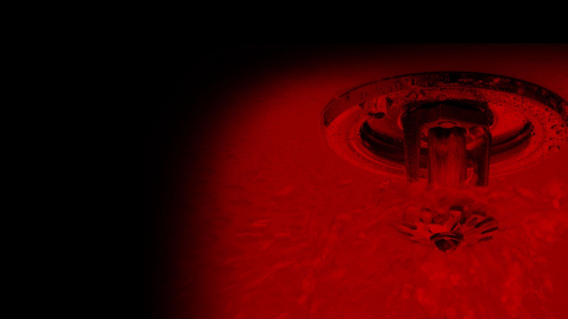 Red-lit fire sprinkler head spraying water against a dark background.