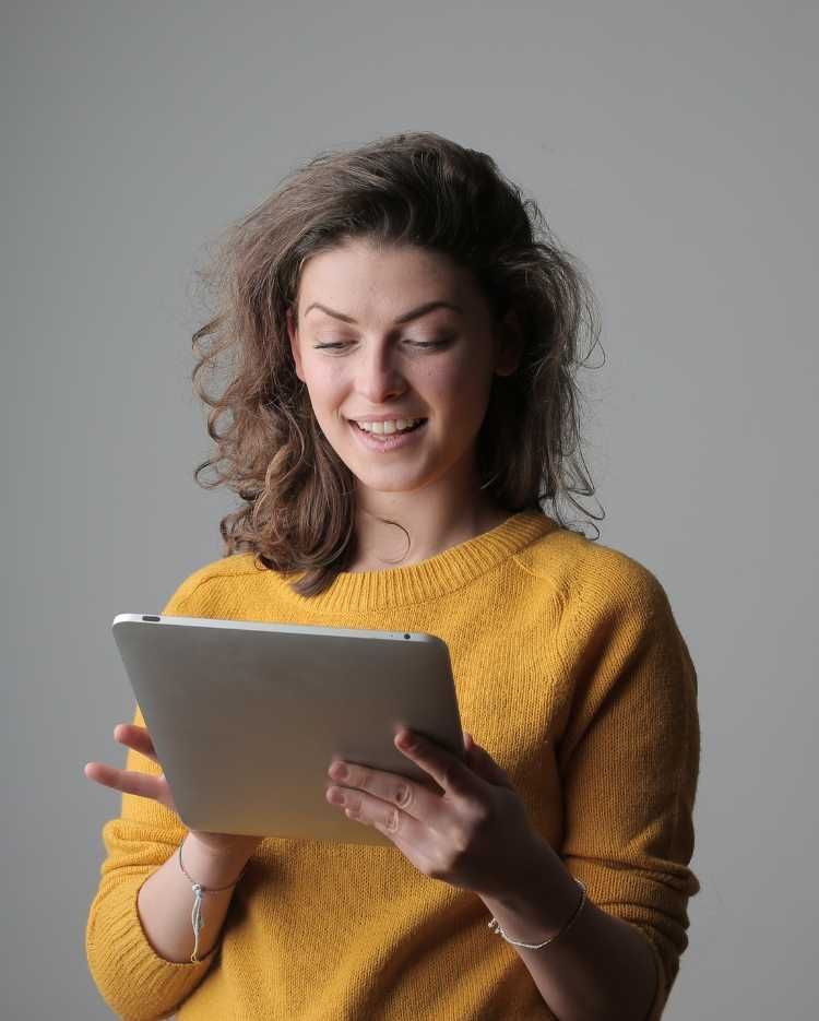 A woman in a yellow sweater is holding a tablet computer.