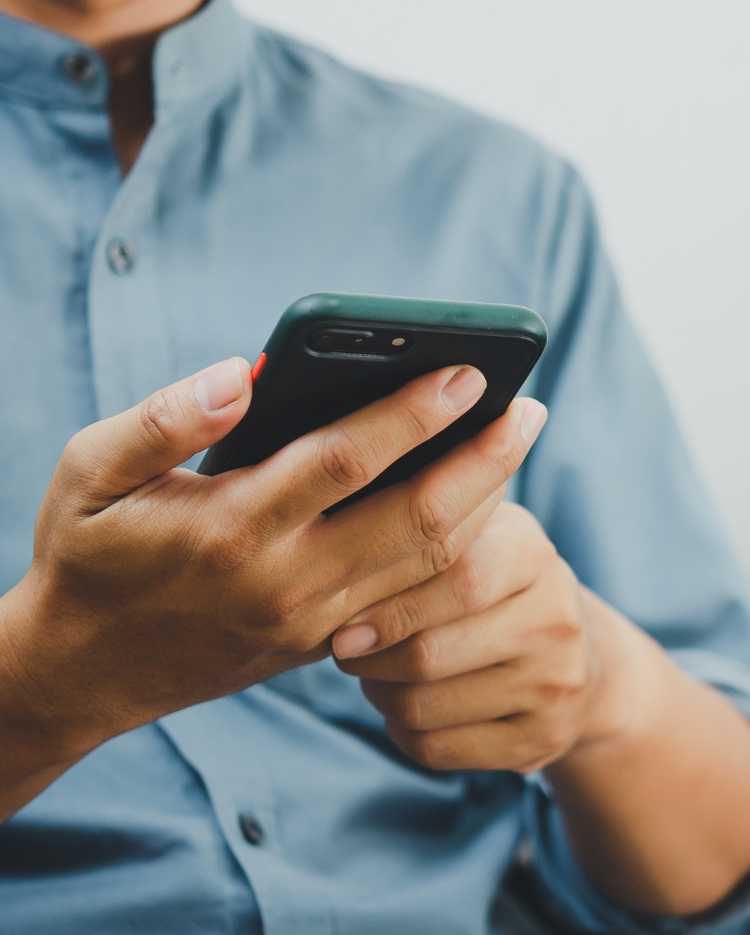 A man in a blue shirt is holding a cell phone in his hands.