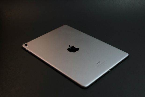 The back of an apple ipad pro is laying on a black surface.