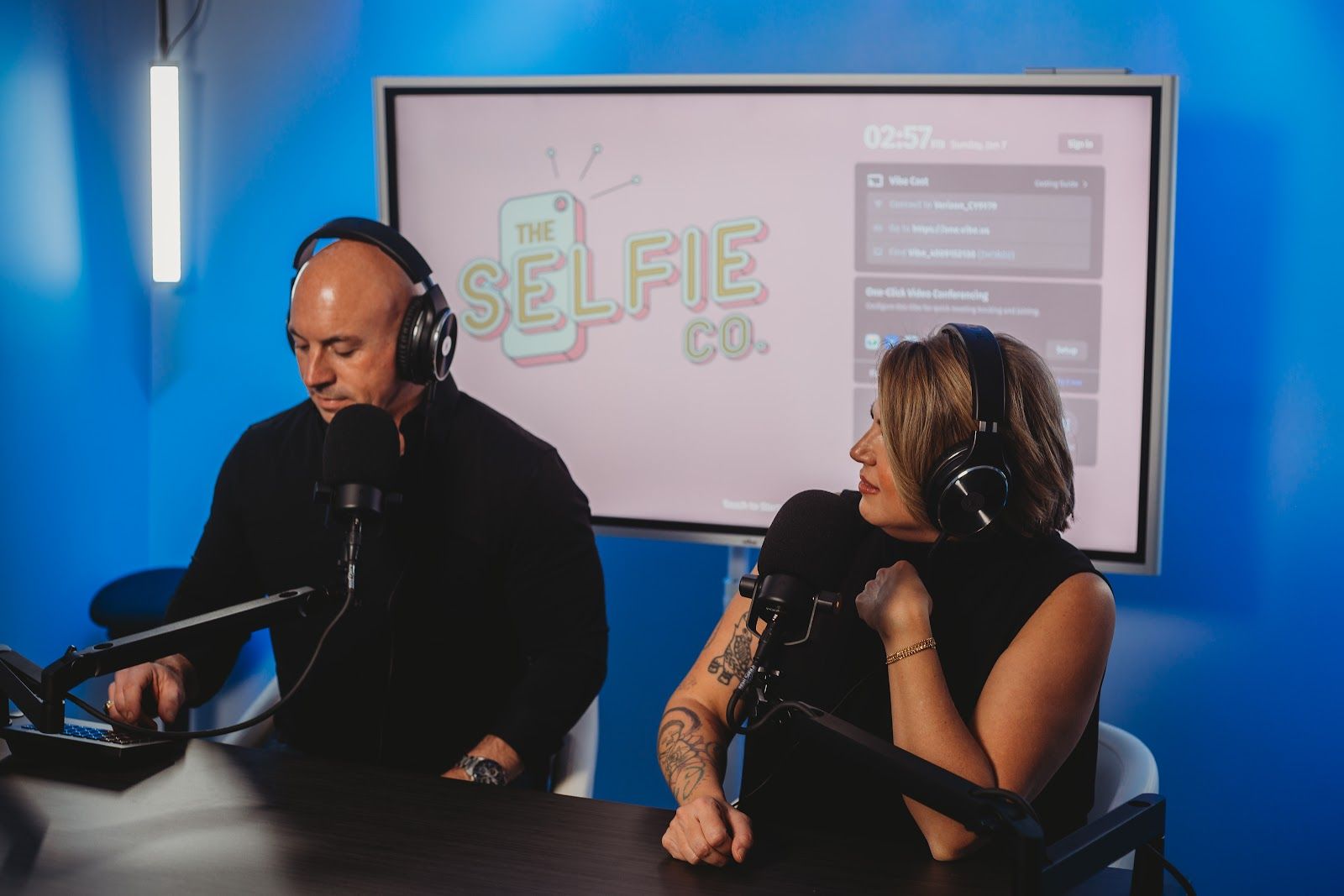 A man and a woman are sitting at a table in front of microphones.