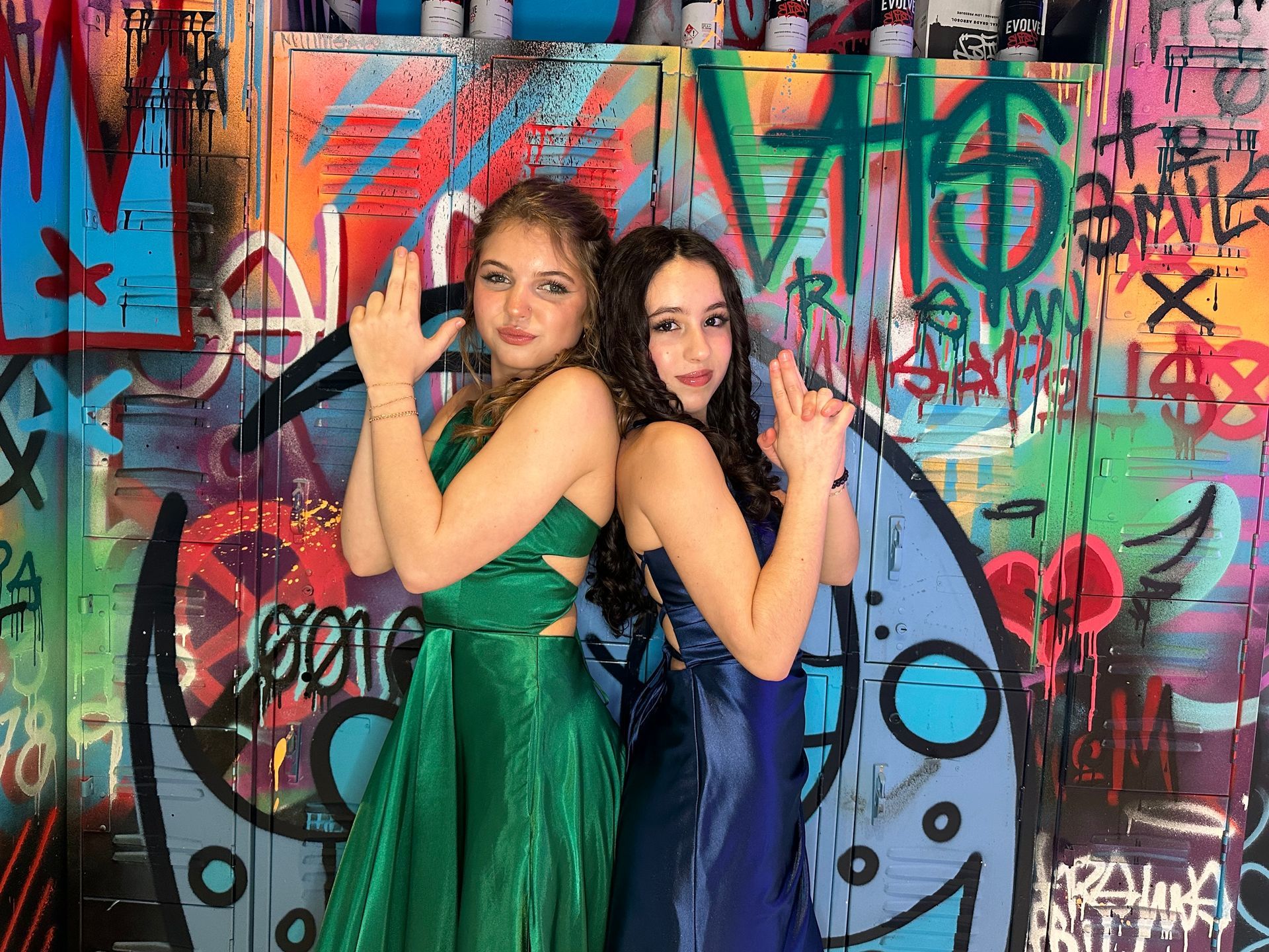 Two girls are posing for a picture in front of a graffiti wall.