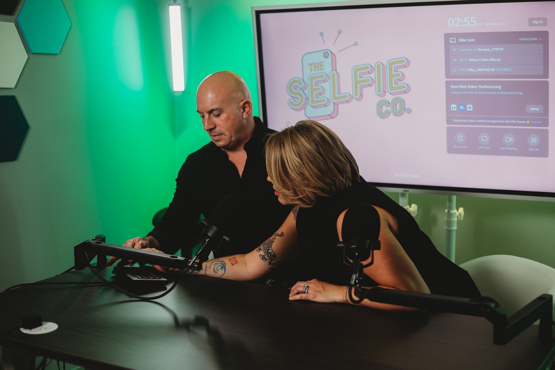 A man and a woman are sitting at a table in front of a microphone.