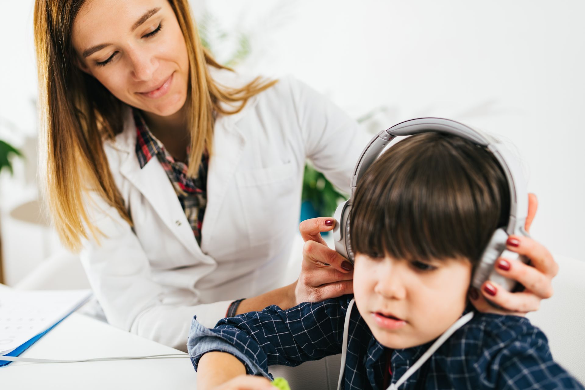 A woman is putting headphones on a young boy 's ears.