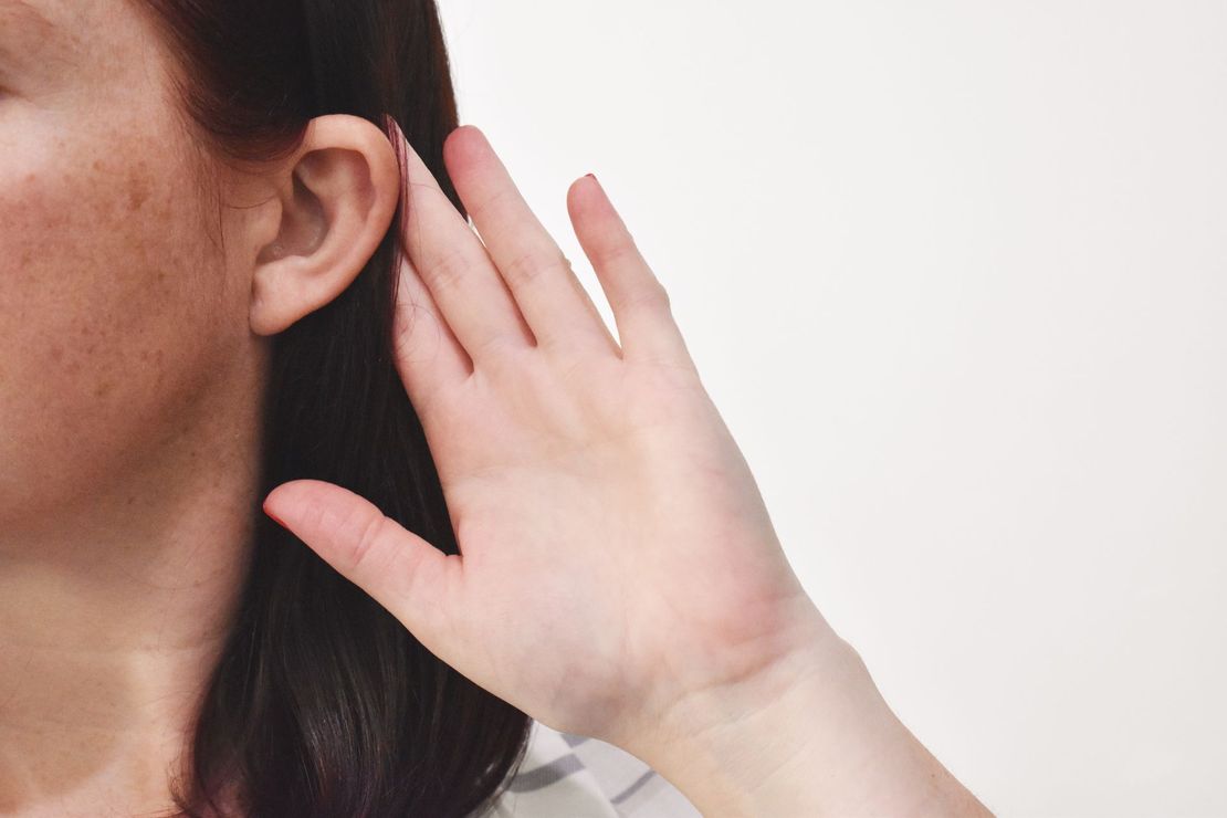 A woman is holding her hand to her ear.