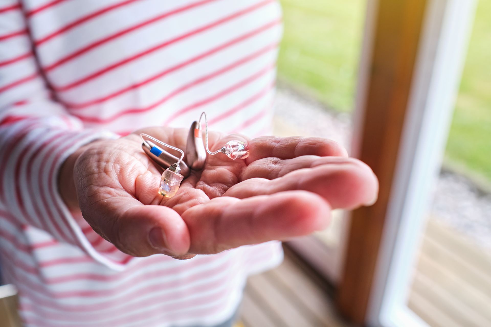 A person is holding a pair of hearing aids in their hand.
