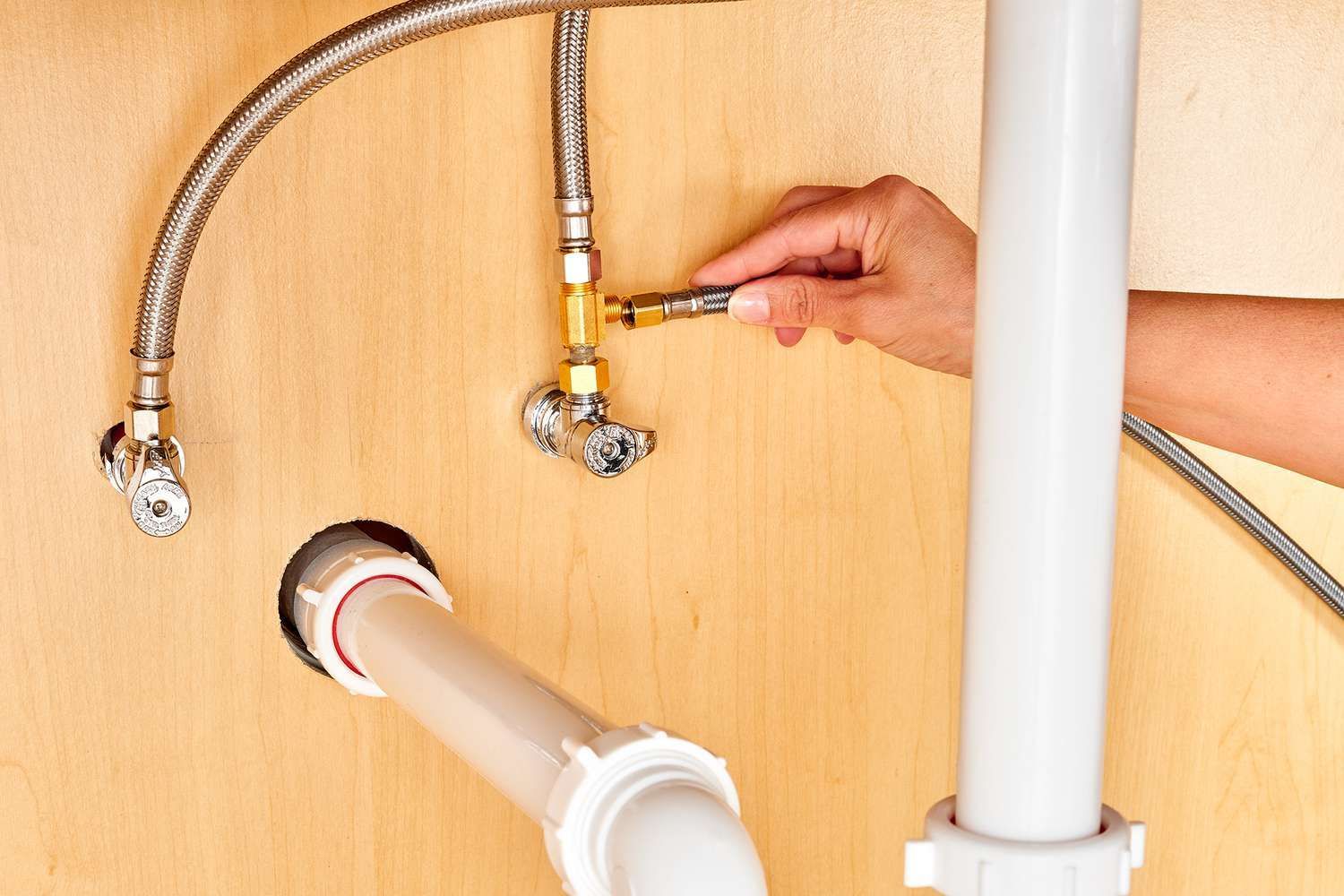 Hand turning valve on plumbing under a sink.