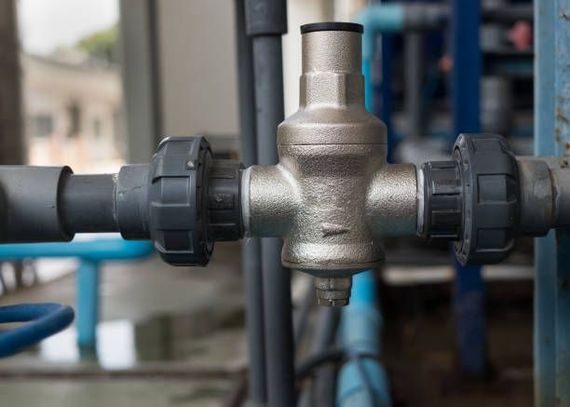 Silver pressure relief valve connected to gray pipes with black fittings.