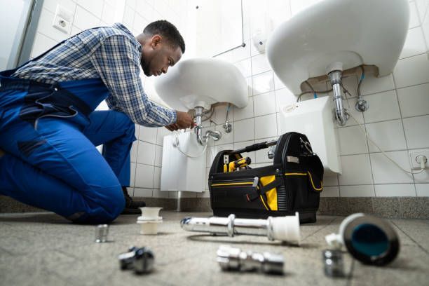 Plumber fixing a white bathroom sink with a toolbox and parts on the floor.
