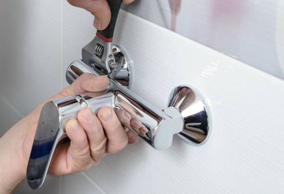 Person uses a wrench to tighten a chrome faucet on a white tiled wall.