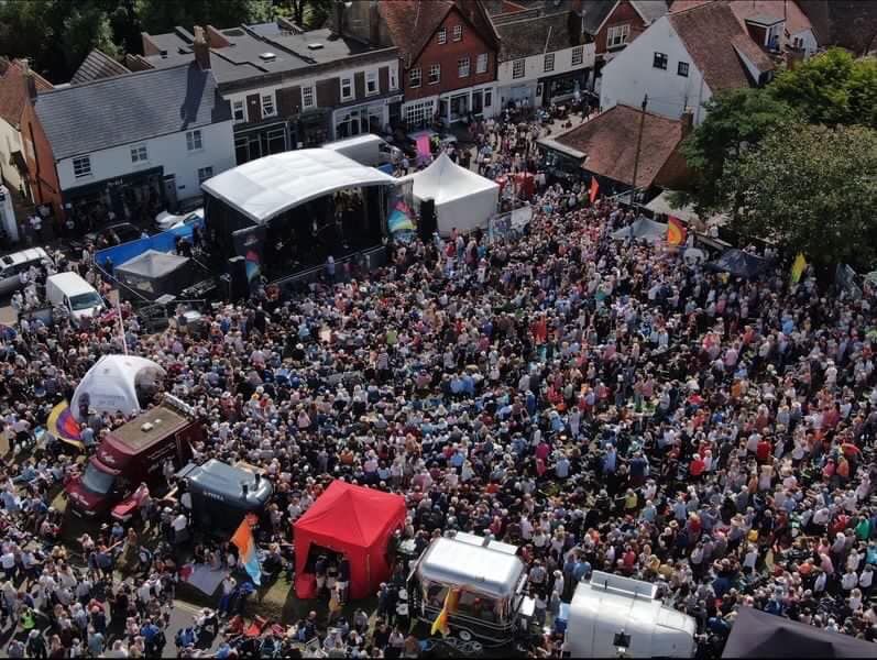 Large outdoor festival crowd gathered near a stage with a white canopy in a town square.
