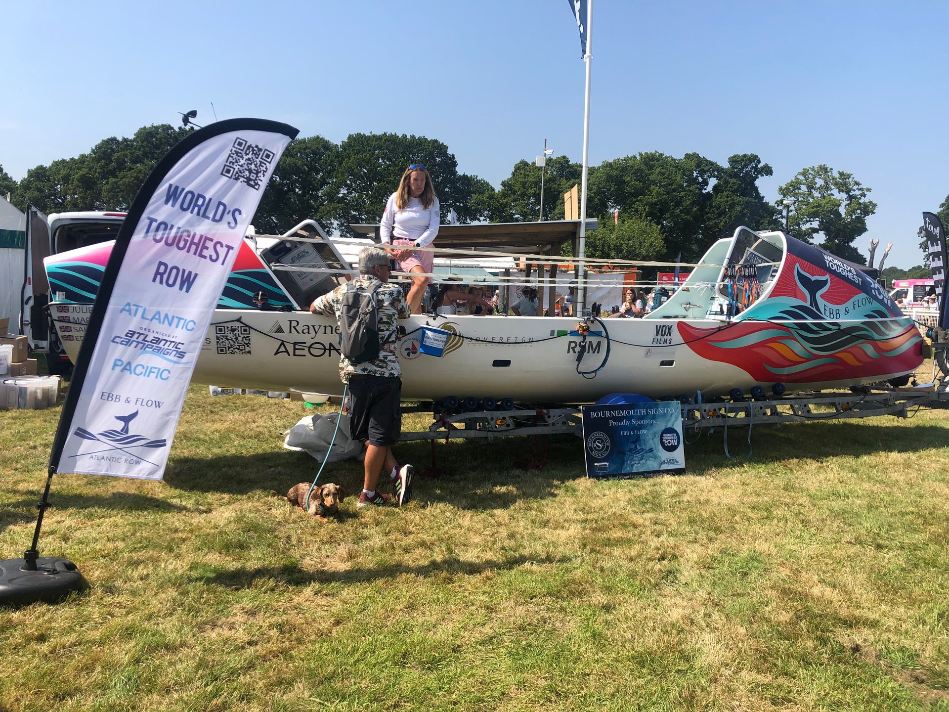 A white boat on a trailer with colorful designs, people nearby, and a flag that says