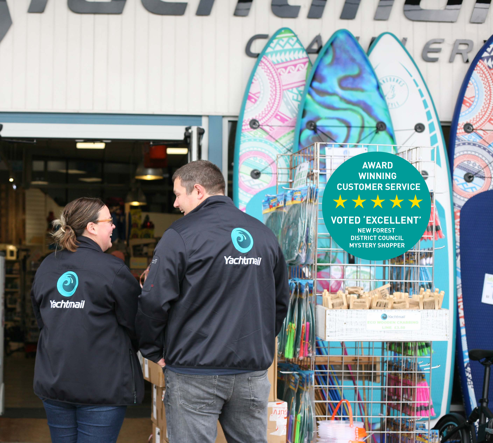 Two people in jackets stand near paddleboards outside a shop.