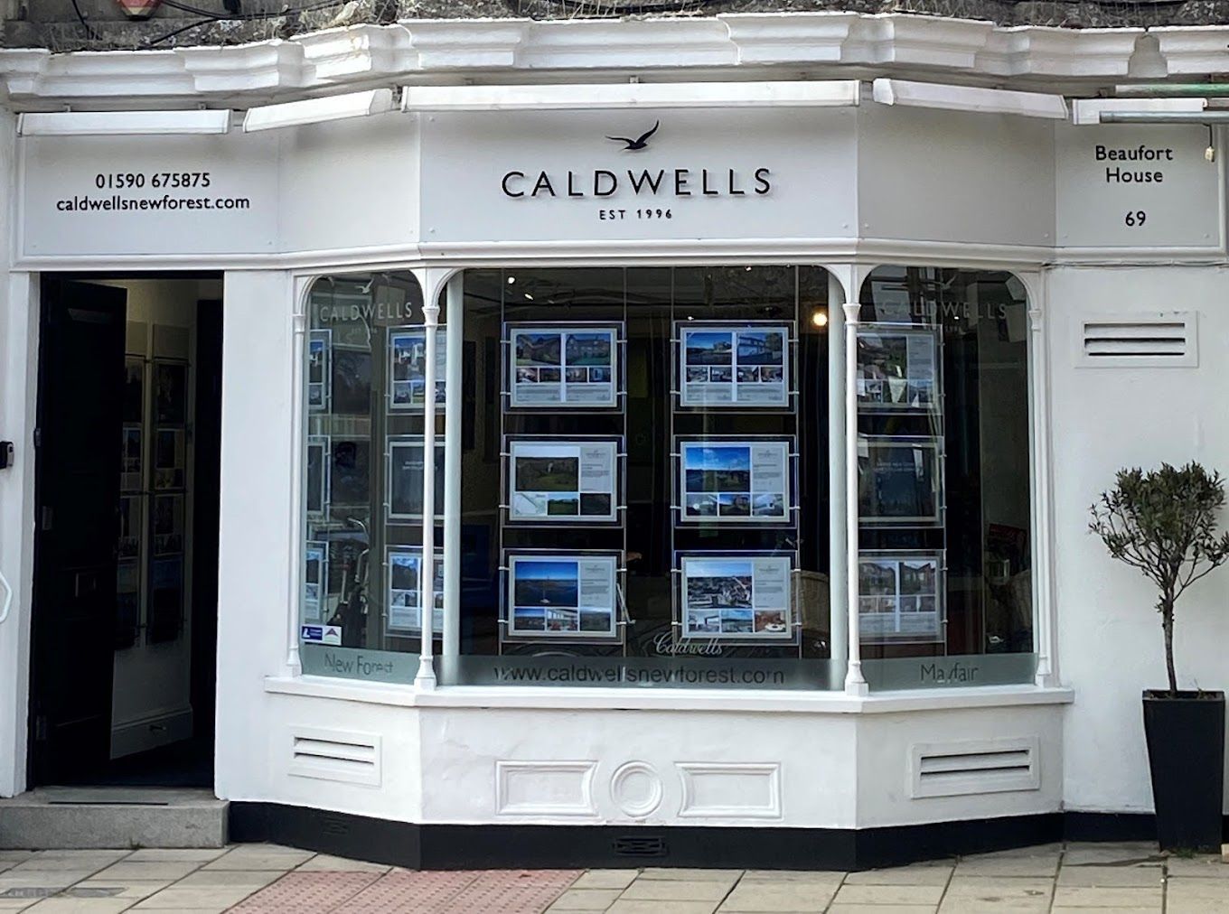 White storefront of Caldwells real estate, showcasing property listings in illuminated windows.